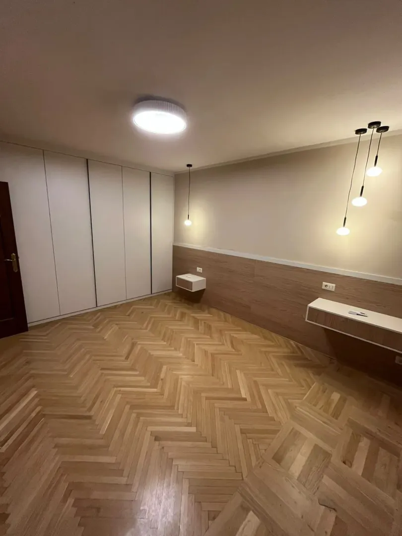 Prazna spavaća soba sa ugradnim plakarom, drvenim parketom i zidnim lampama.