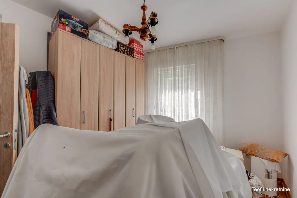 Spavaća soba sa velikim drvenim garderoberom i prekrivenim krevetom.