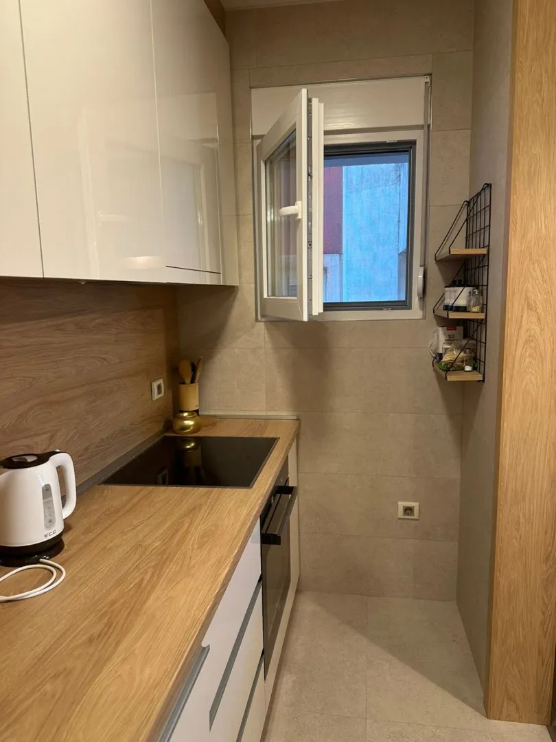 Small kitchen with white cabinets, wooden countertops, and a window.