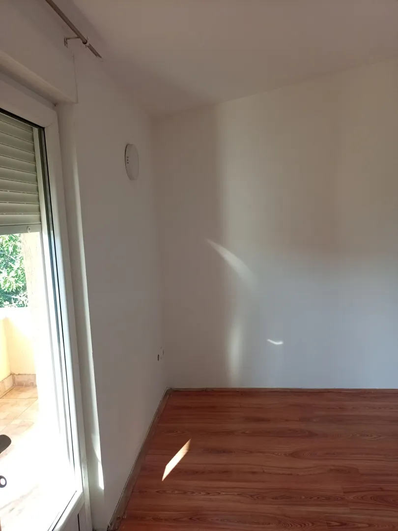 Prazna soba sa drvenim podom i izlazom na terasu.