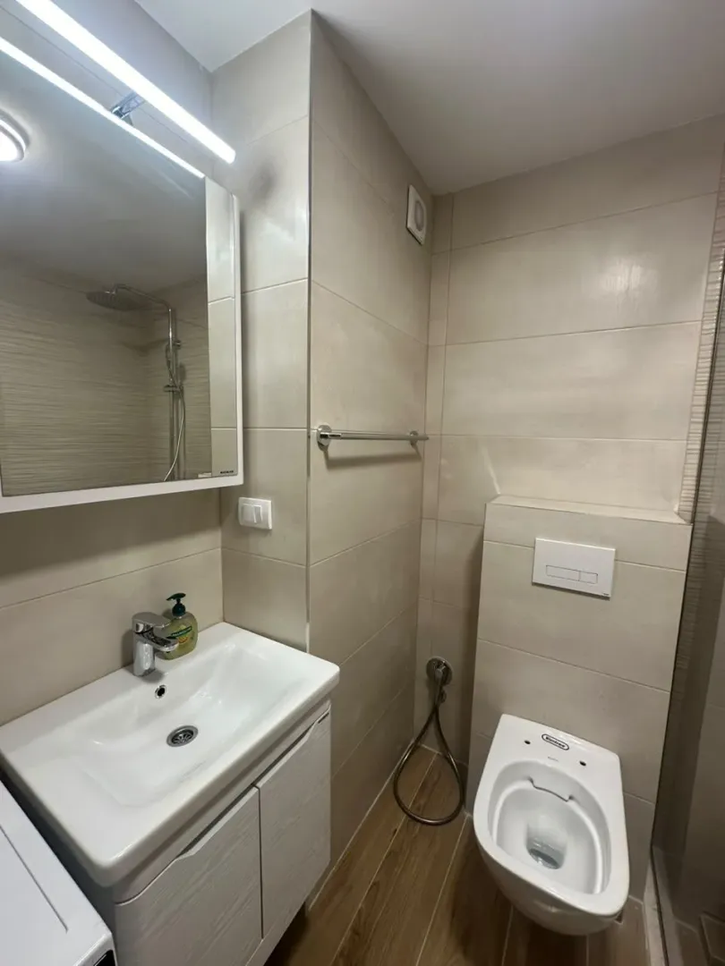 Compact bathroom with a sink, mirror, and toilet in beige tones.