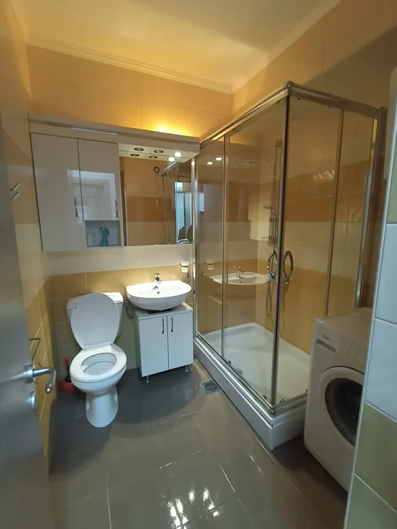 Compact bathroom with a shower cabin, sink, toilet, and washing machine.