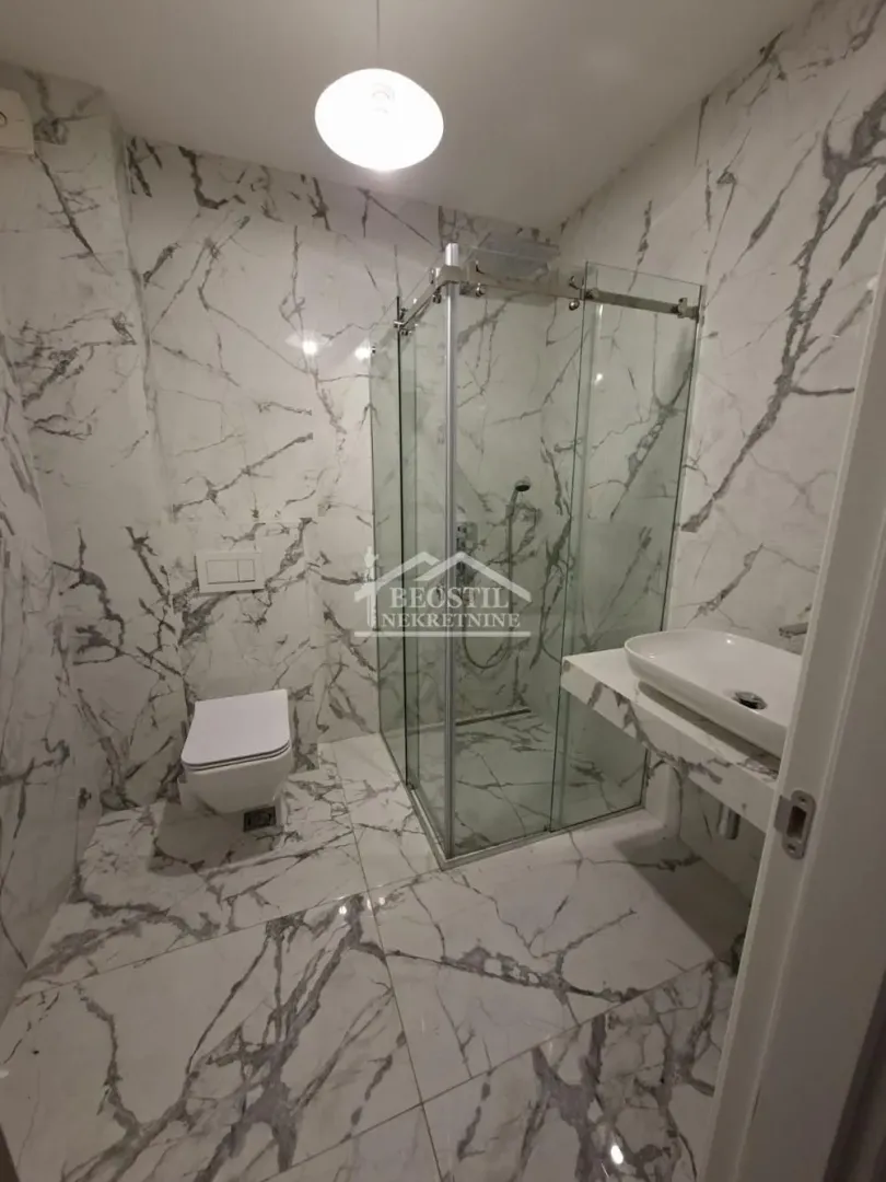 Modern bathroom with a glass shower cabin, sink, and toilet with marble tiles.
