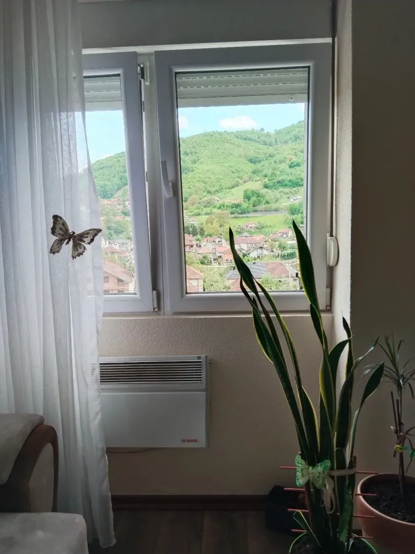 Pogled kroz prozor na okolno naselje i brda.