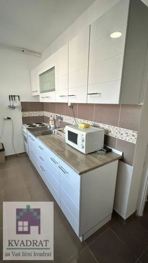 Manja kuhinja sa belim elementima i drvenom radnom pločom.