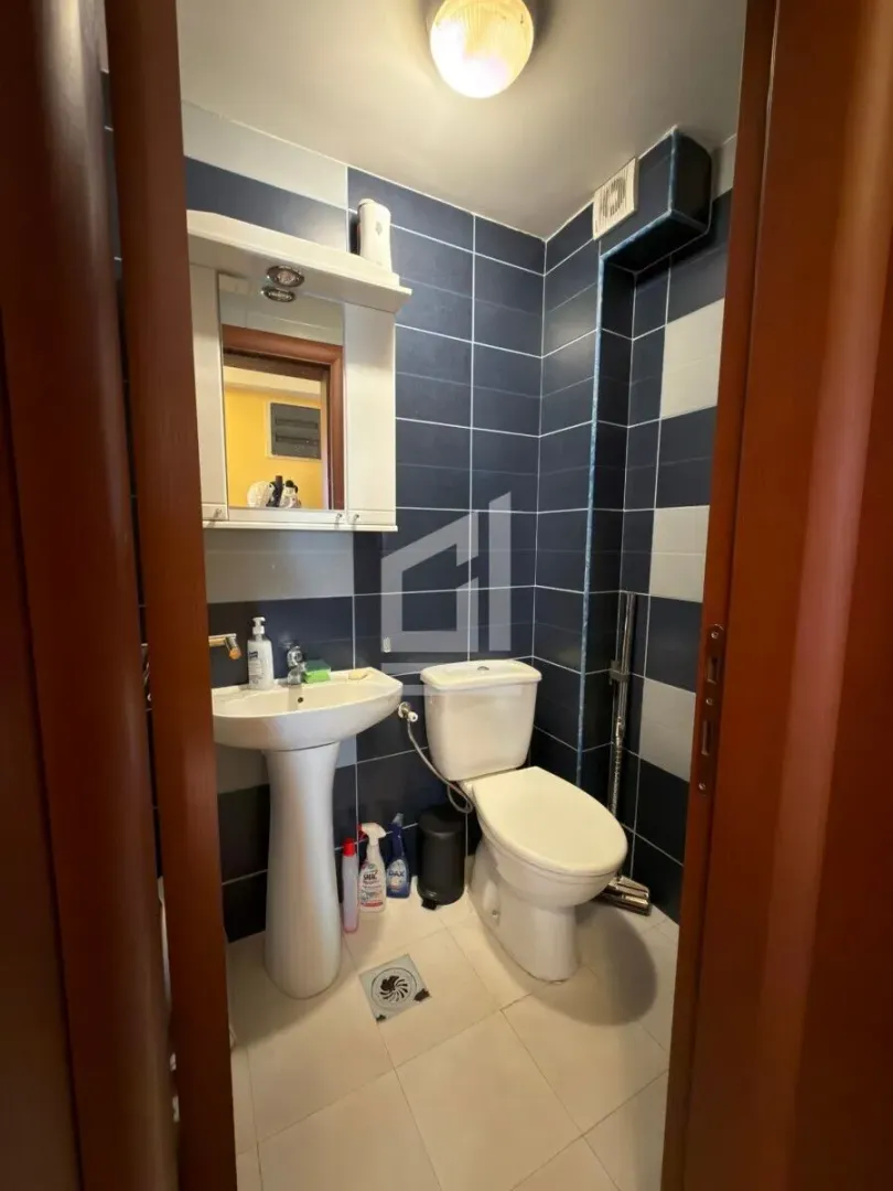 Manje kupatilo sa umivaonikom, WC šoljom i plavim zidnim pločicama.