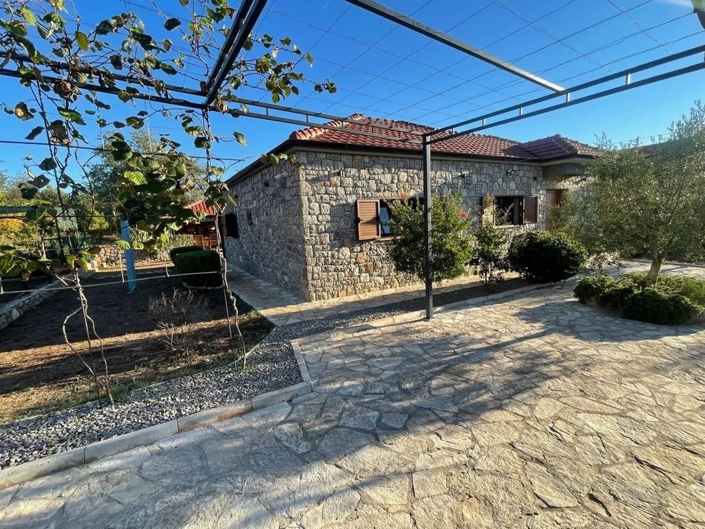 Pogled na dvorište i kamenu kuću sa pergola konstrukcijom.