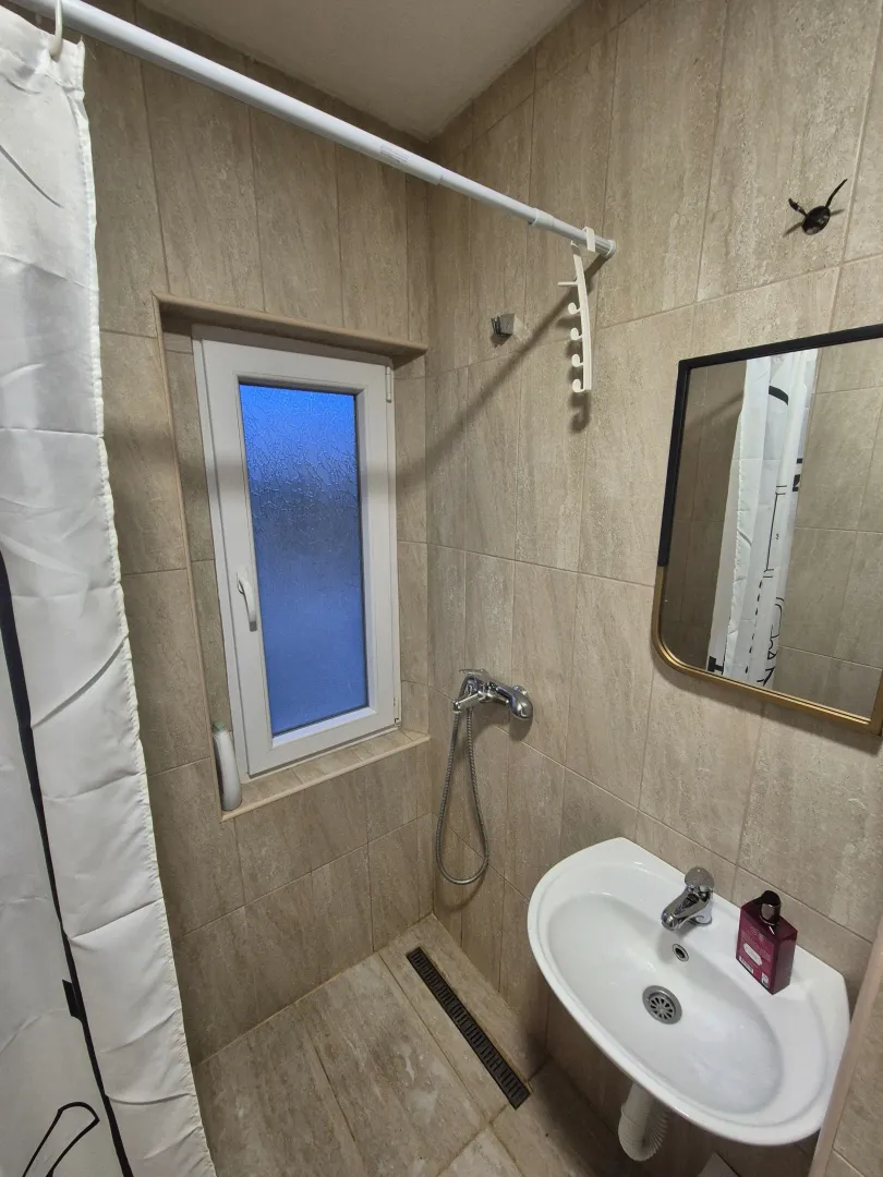 Small bathroom with a walk-in shower area, sink, and a window.