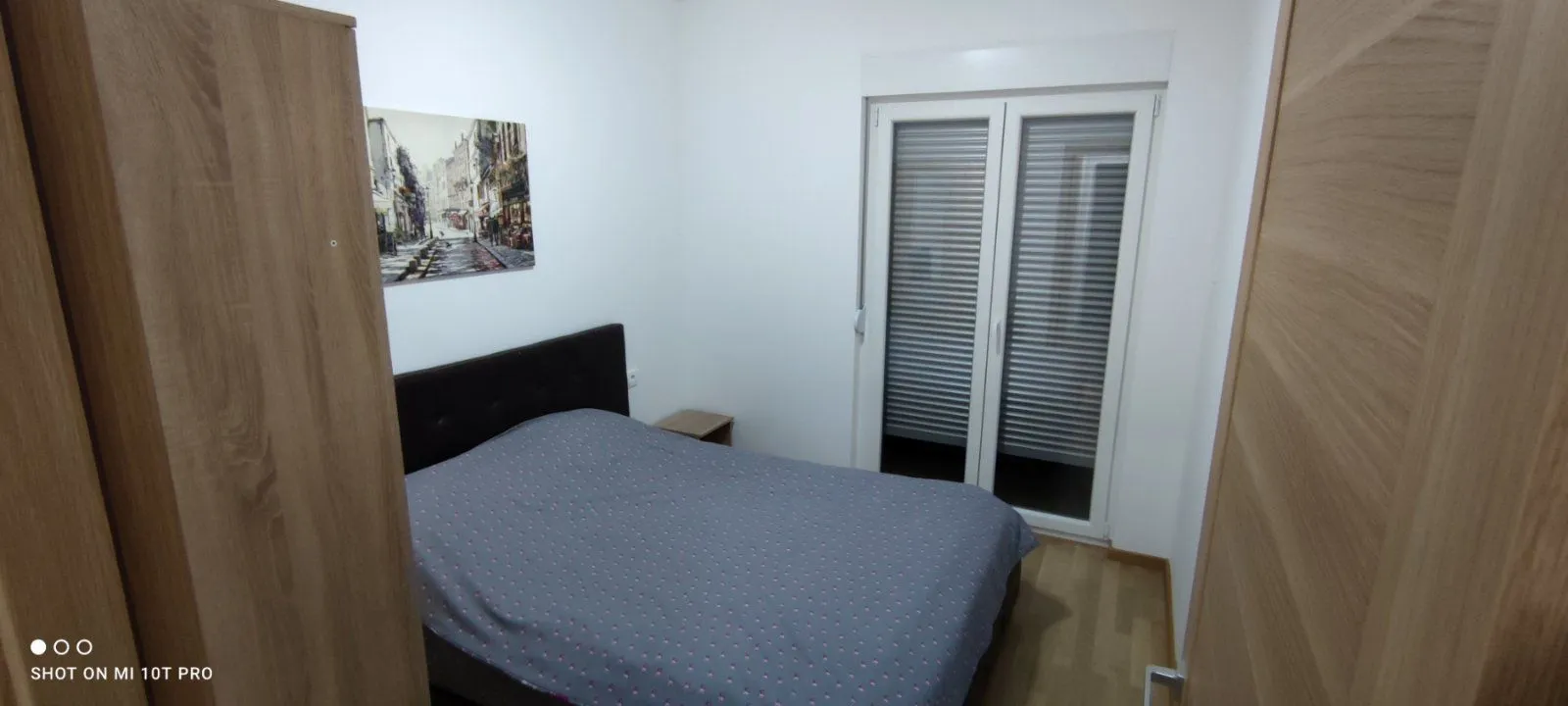 Namještena spavaća soba sa bračnim krevetom, plakarima i izlazom na terasu.