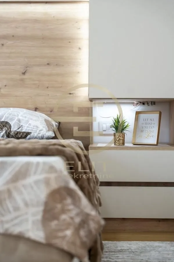 Detalj spavaće sobe sa krevetom, drvenim uzglavljem i ugradnim noćnim stočićem.