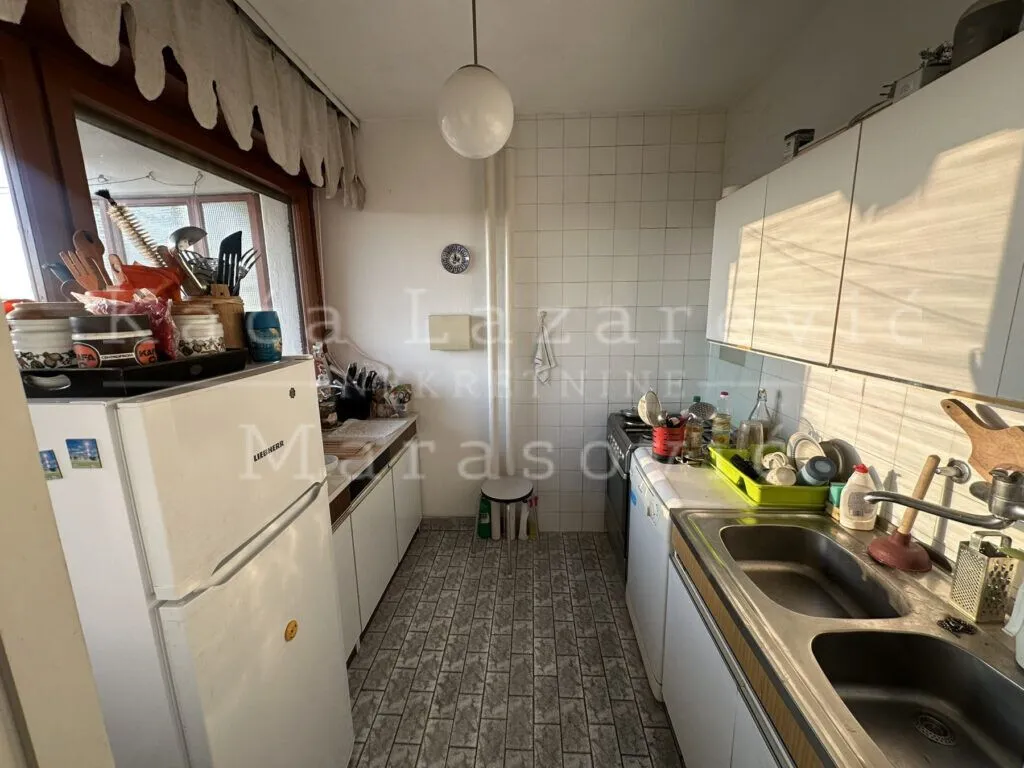 Manja kuhinja sa belim elementima, sudoperom i frižiderom.