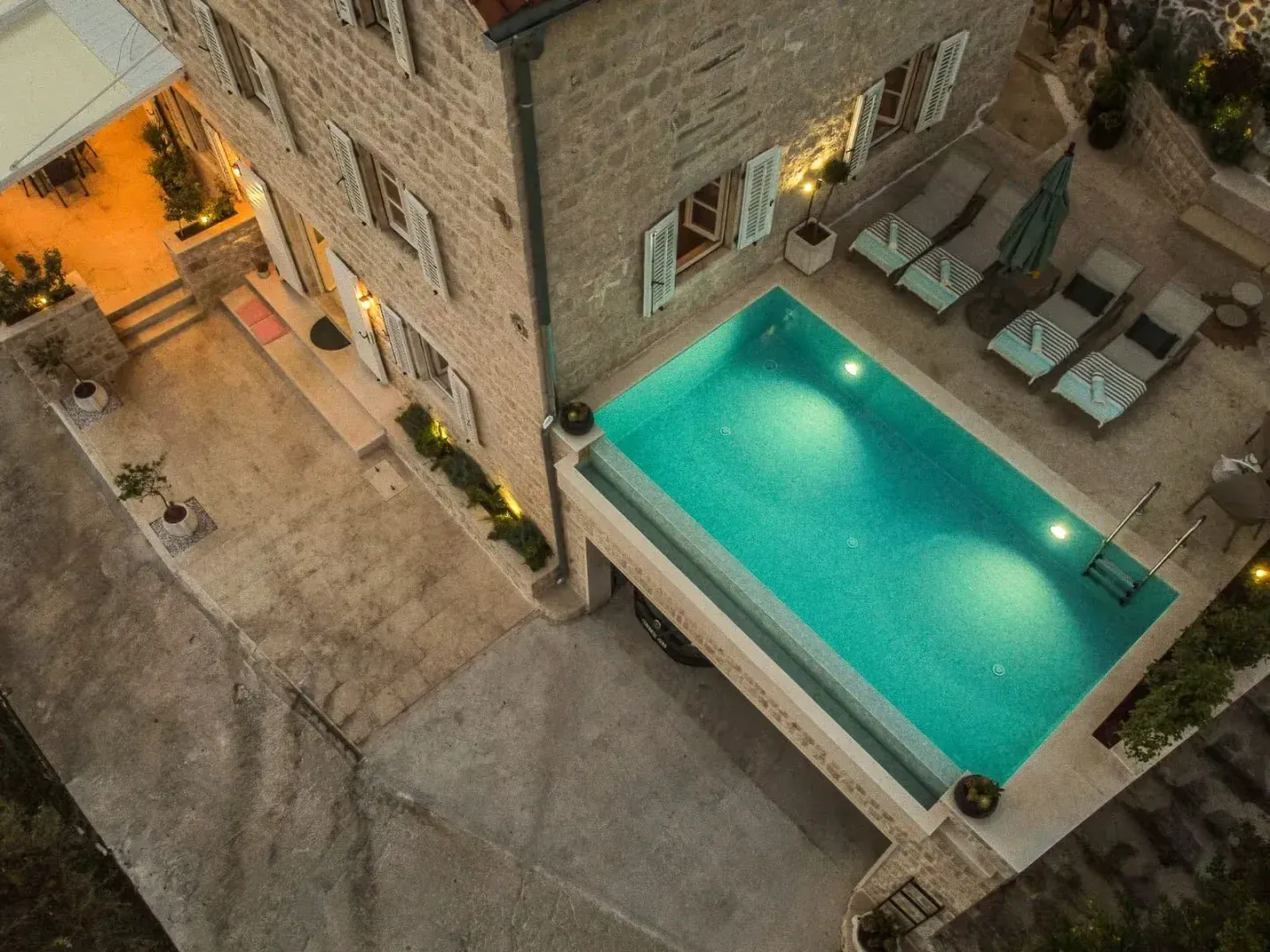Aerial view of a stone house with a swimming pool and landscaped courtyard at night.