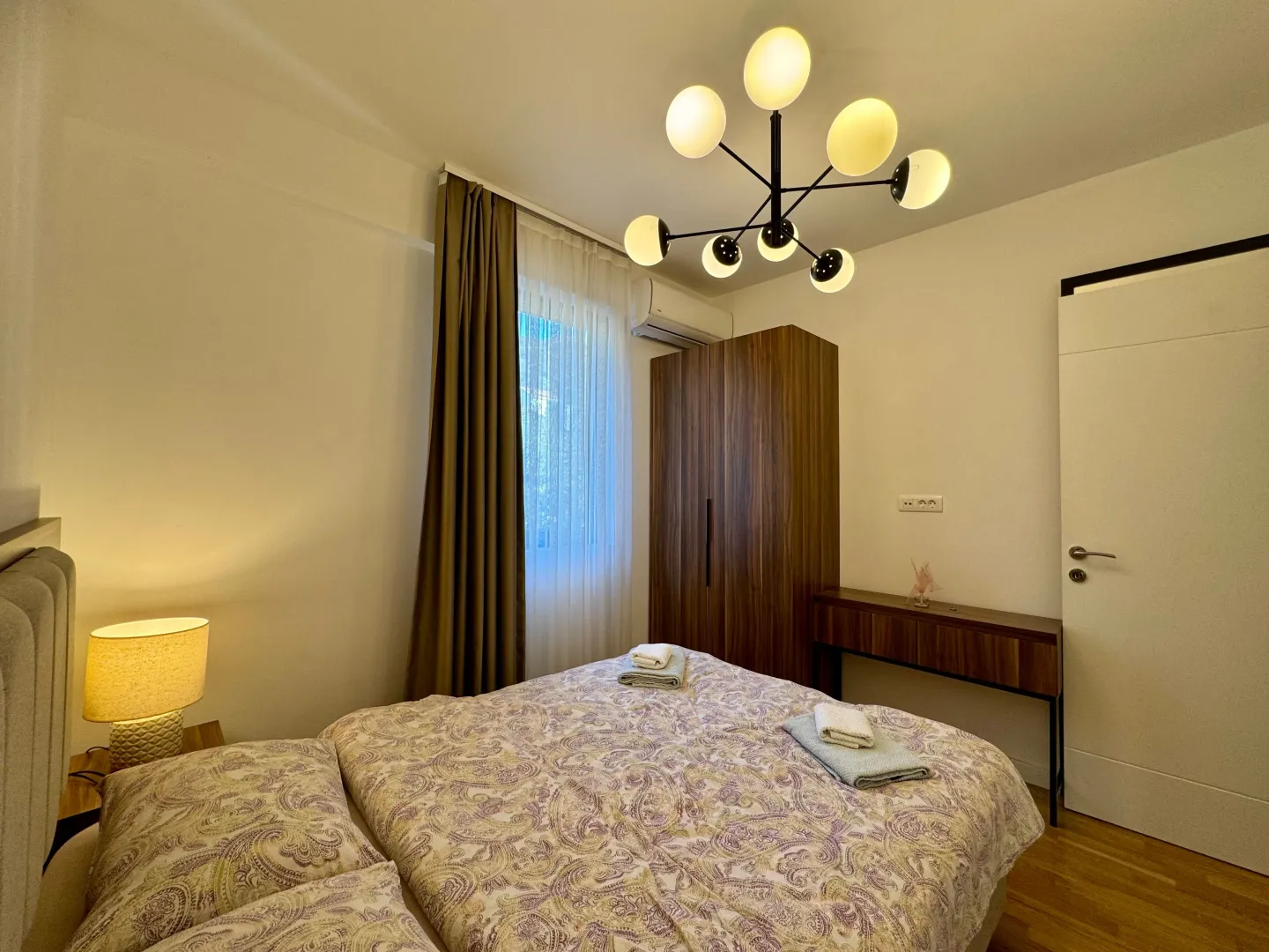 Furnished bedroom with a double bed, wardrobe, and a modern chandelier.