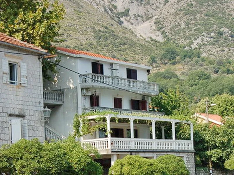 Vanjski izgled višespratne kuće okružene zelenilom u podnožju brda.