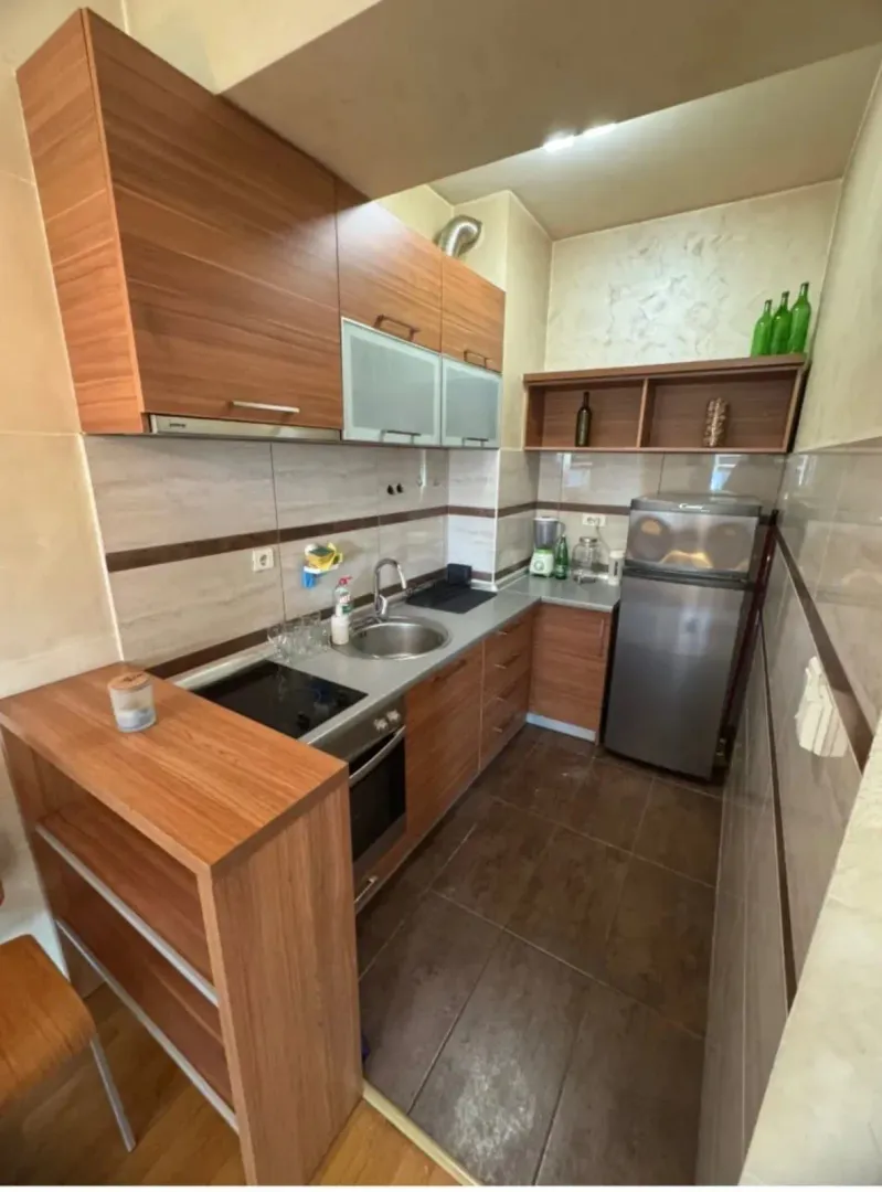 Small wooden kitchen with built-in appliances and a refrigerator.