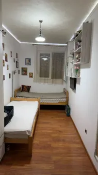 Manja spavaća soba sa dva kreveta i policama na zidu. - image 10
