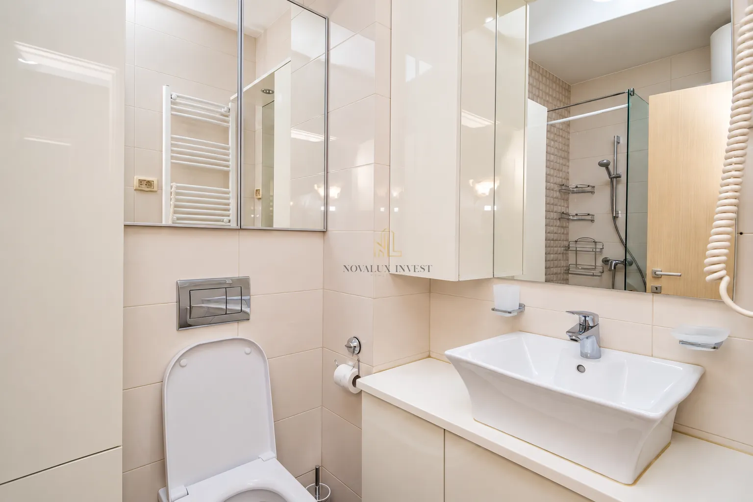Compact bathroom equipped with a washbasin, toilet, and a shower cabin in beige tones.