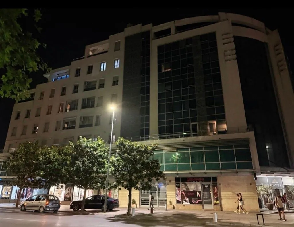 Noćni prikaz fasade stambeno-poslovne zgrade sa ulicom u prvom planu.