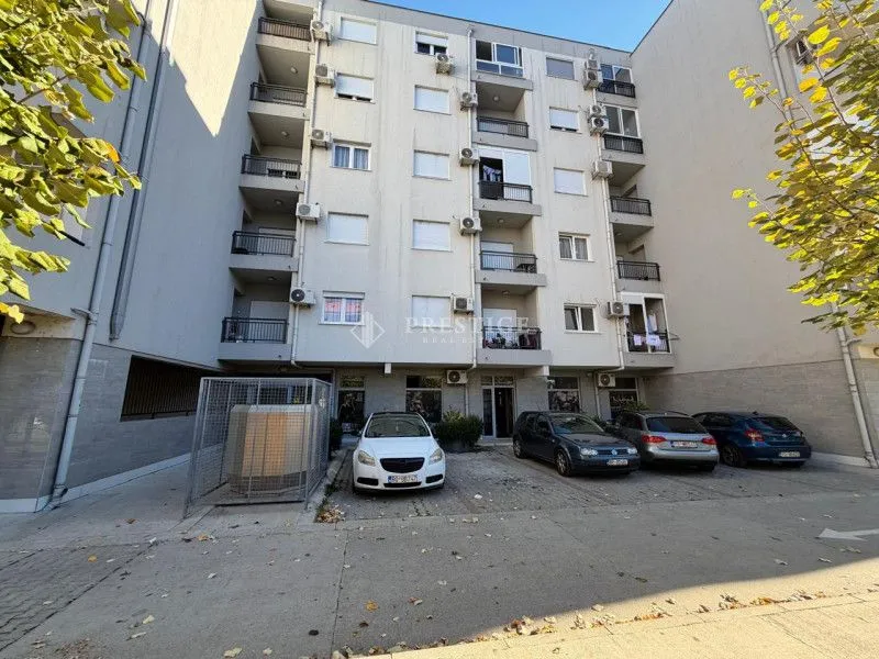 Spoljašnji izgled stambene zgrade sa parkingom ispred.