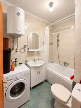 Small bathroom with a bathtub, washbasin, washing machine, and water heater. - image 3