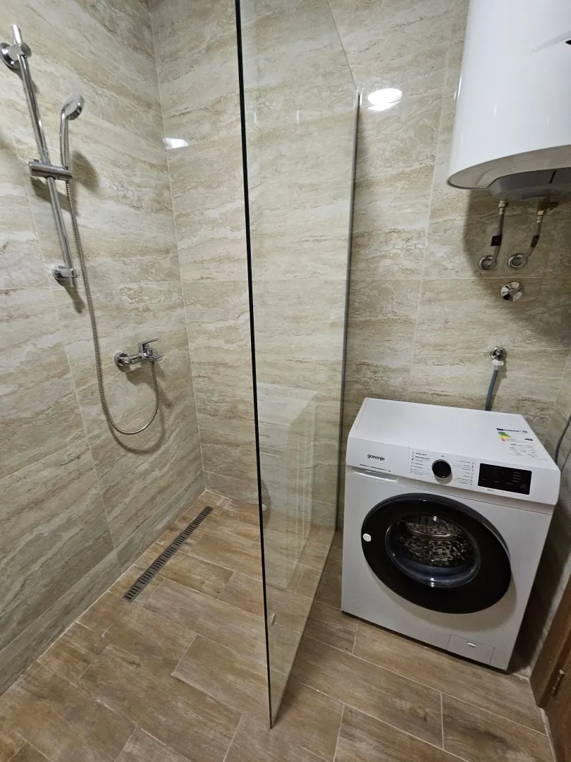 Moderno opremljeno kupatilo sa tuš kabinom i veš mašinom.