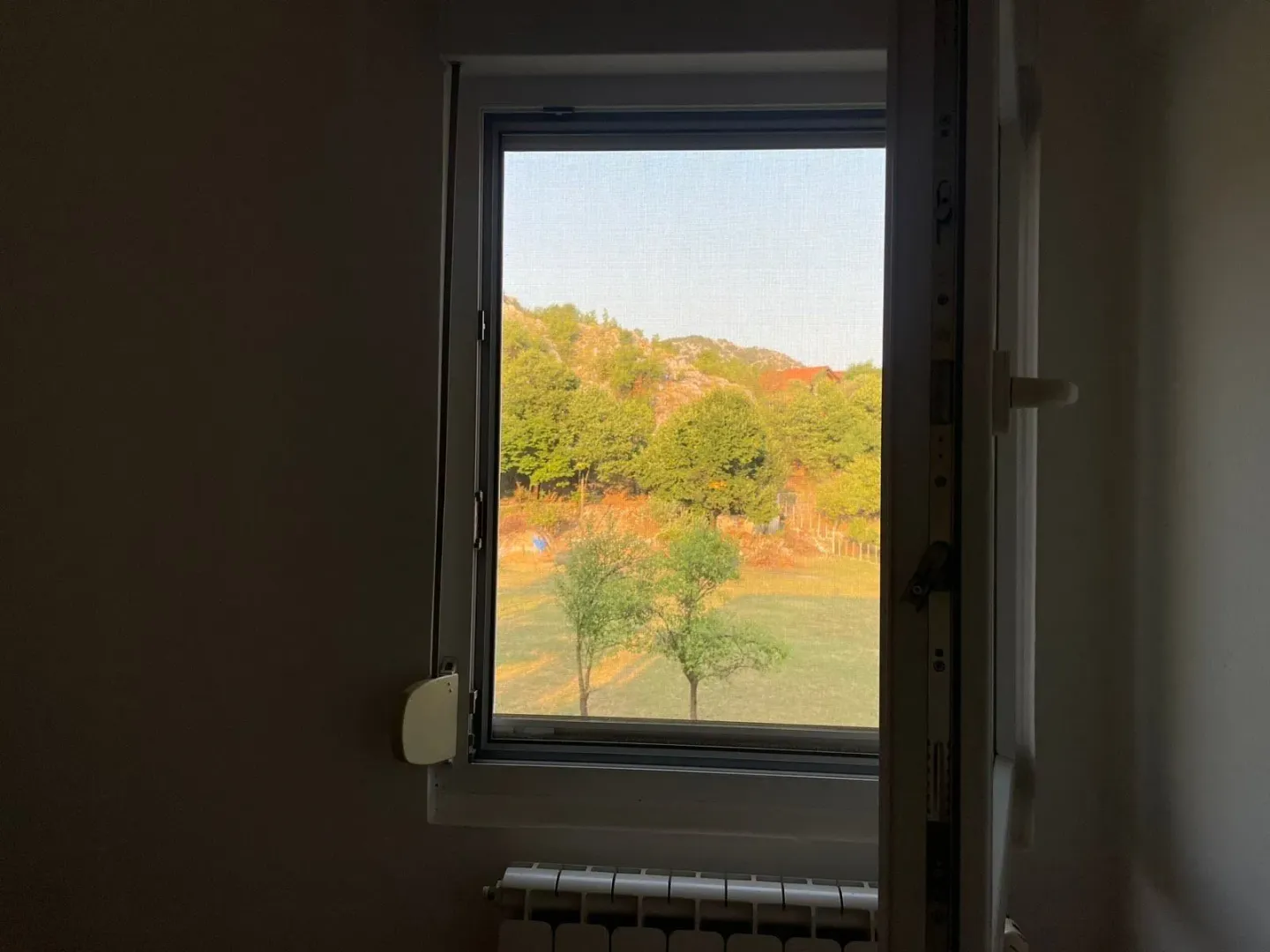 Pogled kroz prozor na zelene površine i brda.