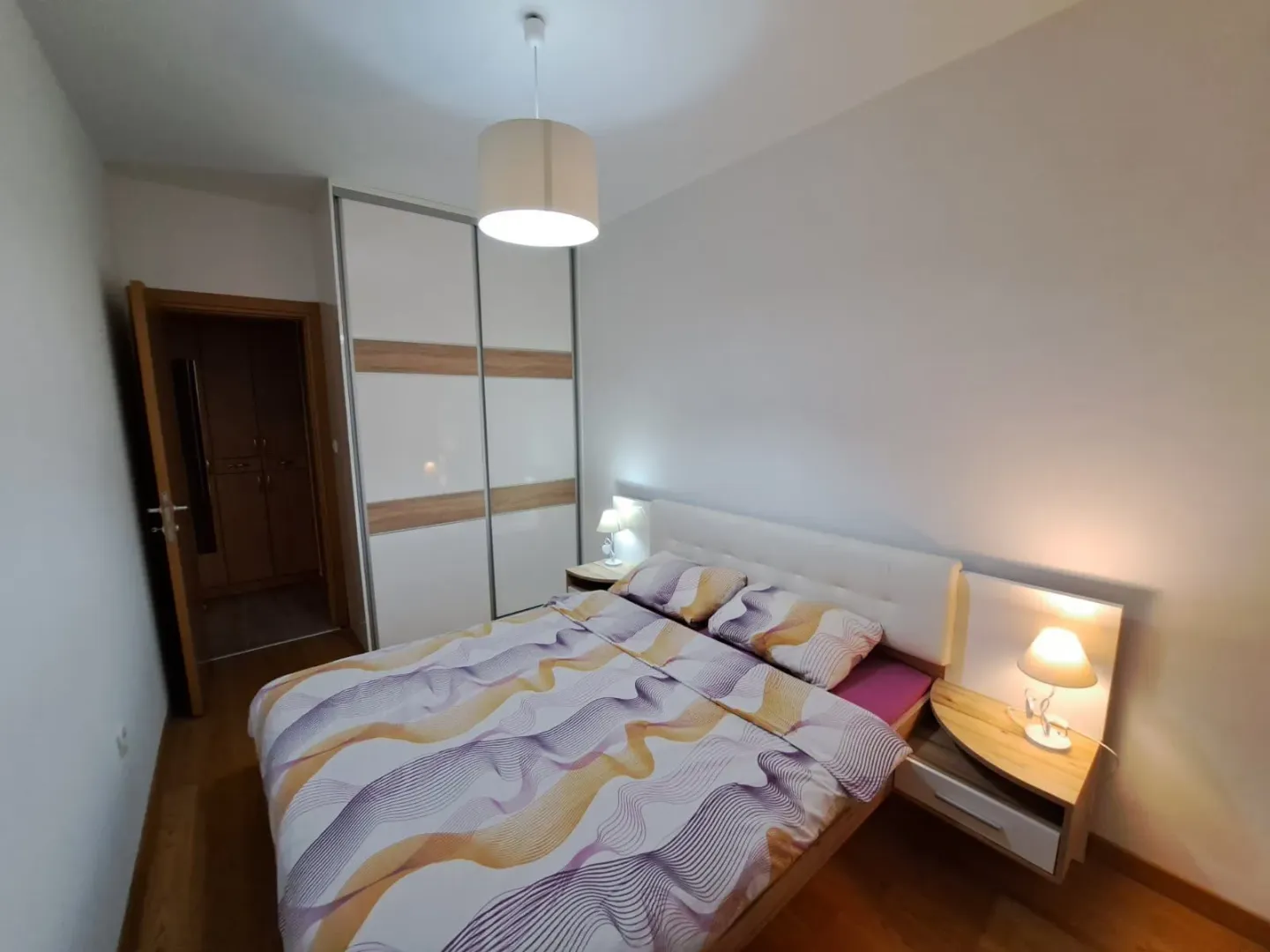 Namještena spavaća soba sa bračnim krevetom, plakarom i noćnim stočićima.