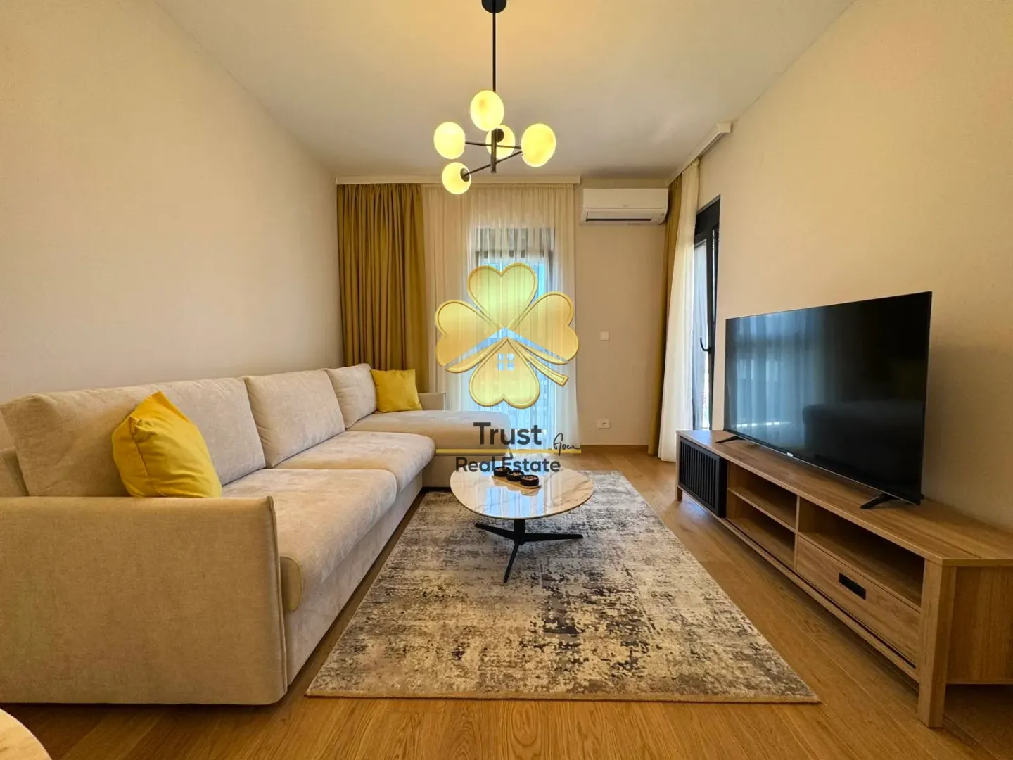 Dnevna soba sa garniturom, TV komodom i modernim lusterom.