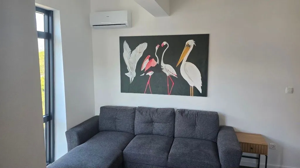 Dnevni boravak sa sivom ugaonom garniturom i umjetničkom slikom na zidu.