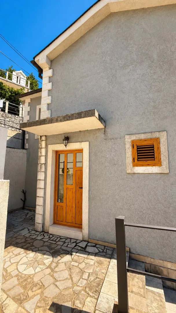 Eksterijer kuće sa drvenim ulaznim vratima i popločanim dvorištem.