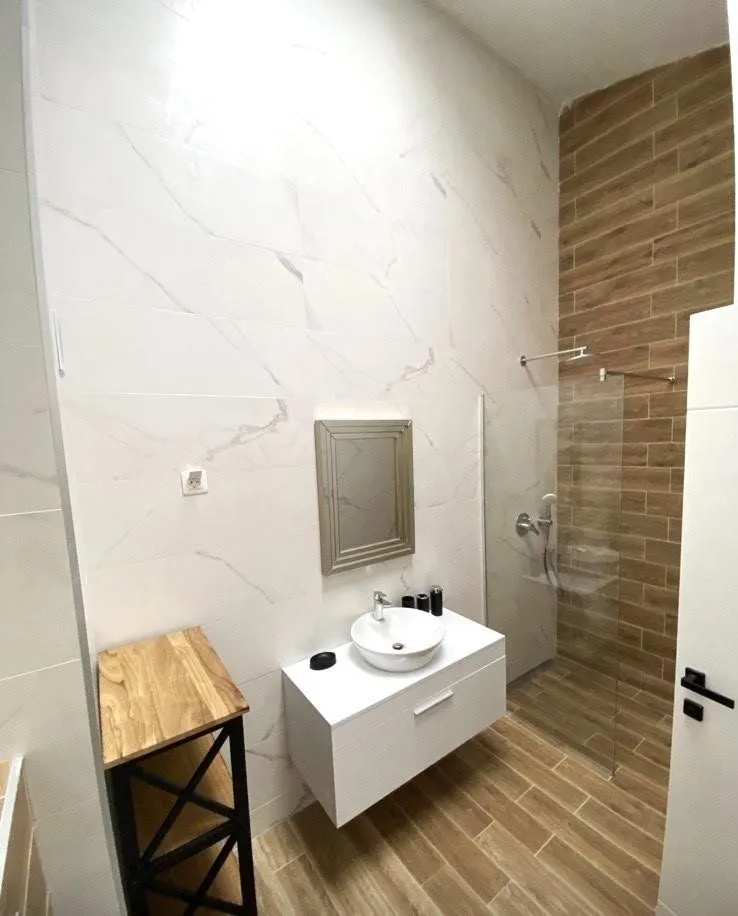 Moderne kupatilo sa tuš kabinom, umivaonikom i pločicama u imitaciji drveta.