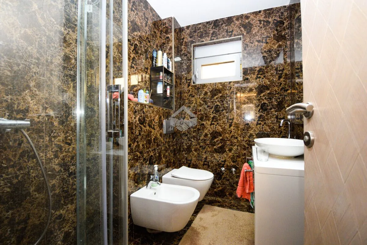 Bathroom lined with marble tiles featuring a shower cabin, washbasin, and sanitary fixtures.