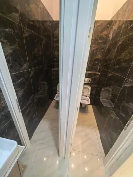 View of two bathrooms with dark tiles and toilets. - image 3