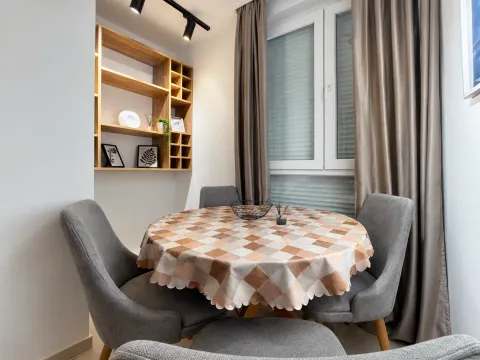 Dining area with a round table, grey chairs, and a wooden wall shelf. - image 4