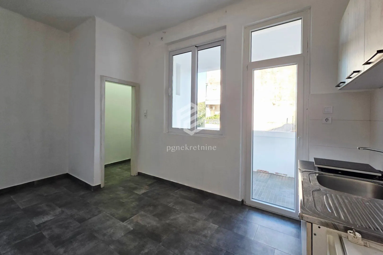 Small kitchen with access to the terrace and dark floor tiles.