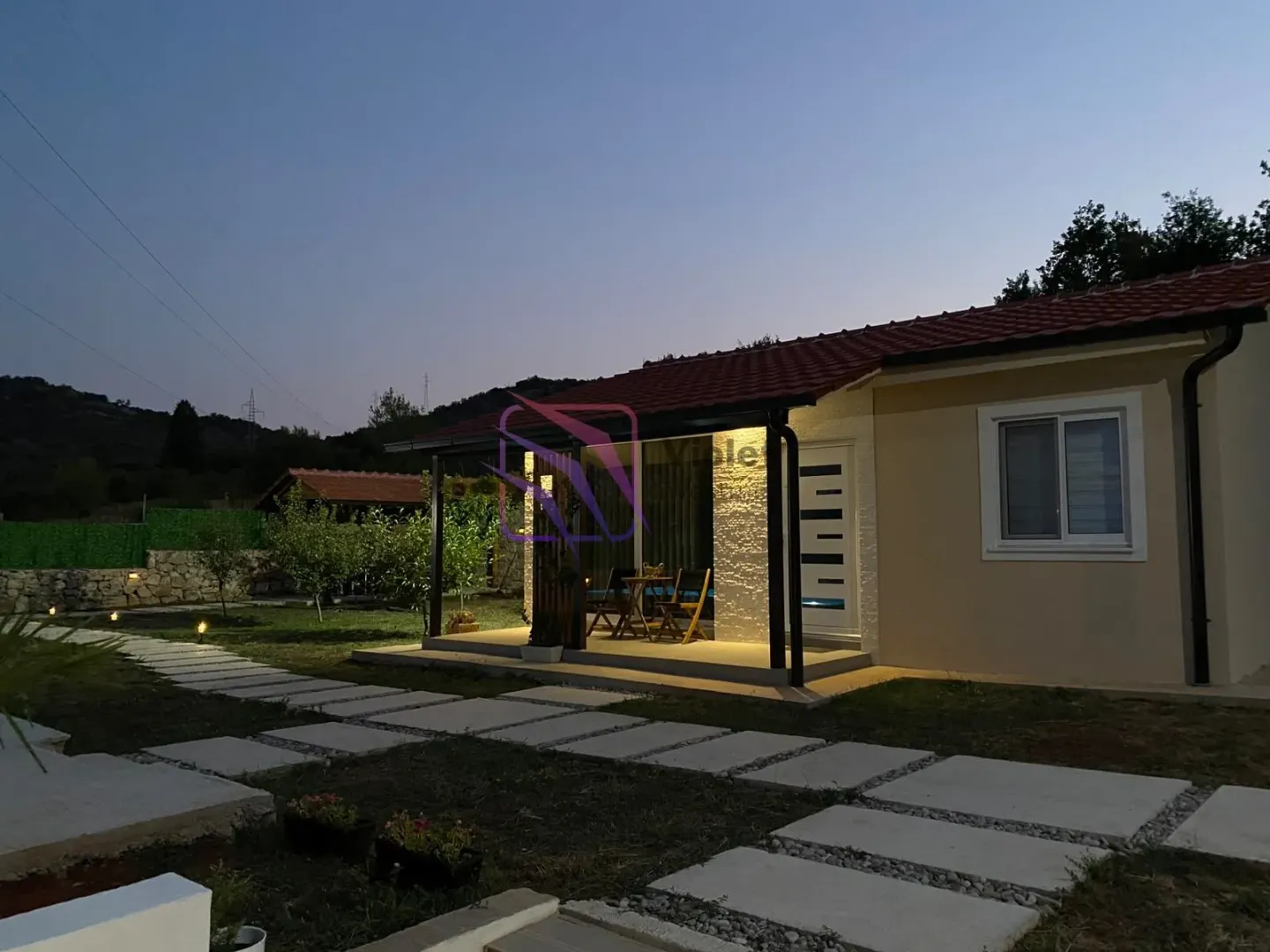 Exterior view of the house with an illuminated covered terrace at dusk.
