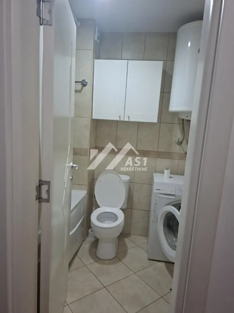 Pogled na kupatilo sa WC šoljom, mašinom za veš i pločicama.