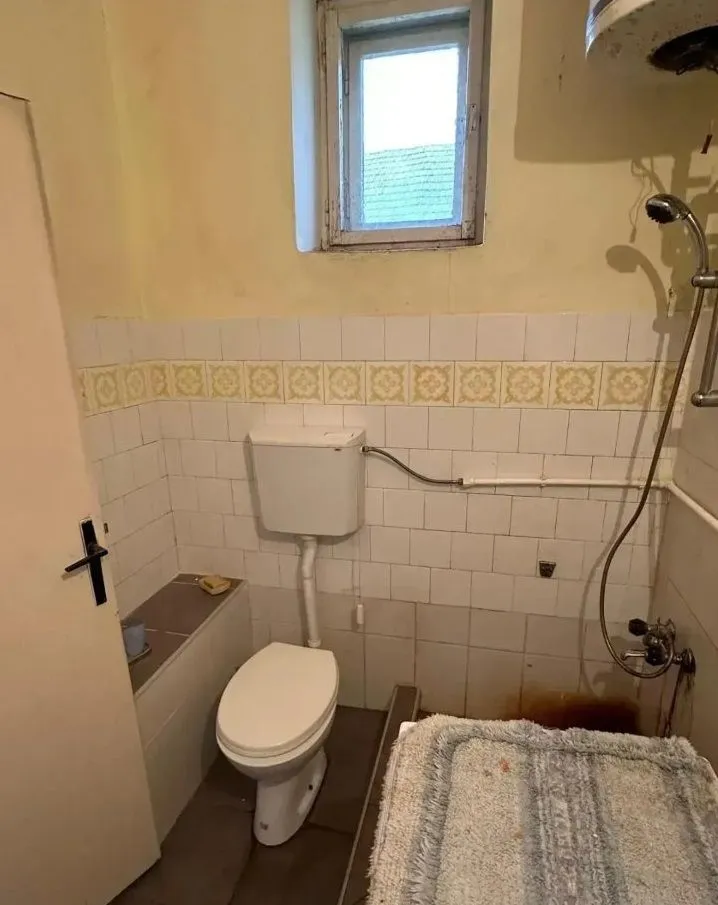 Starije kupatilo sa kadom, WC šoljom i malim prozorom.