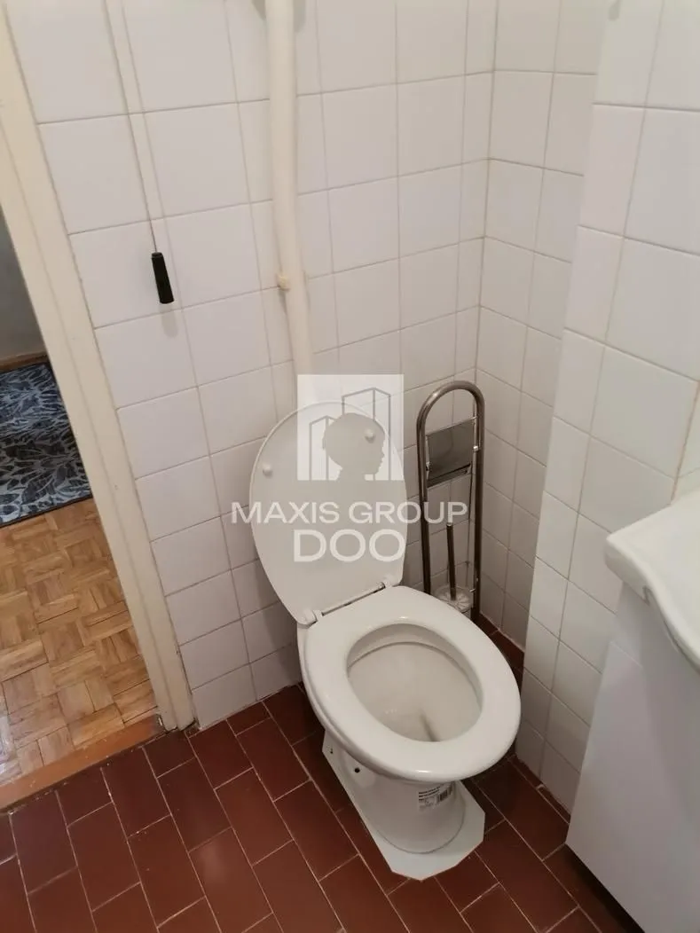 Manje kupatilo obloženo belim pločicama sa toaletom.