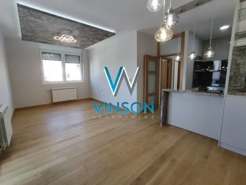 View of a bright living room with hardwood floors and a kitchen in the background. - image 3