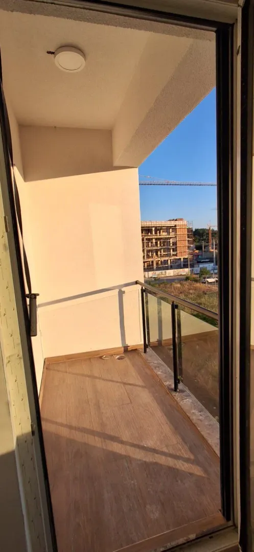 Pogled na nenamješten balkon sa staklenom ogradom i drvenom podnom oblogom.
