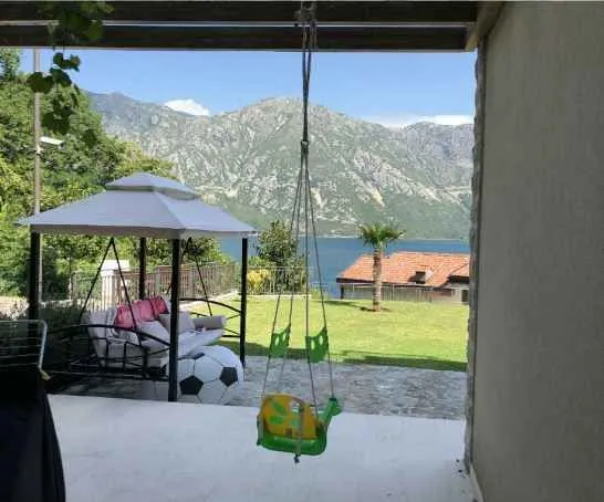 Pogled sa natkrivene terase na dvorište sa ljuljaškom, more i planine.