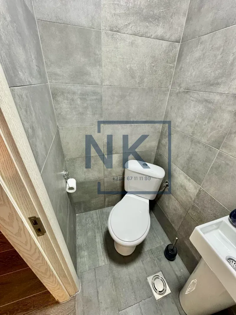 Manje kupatilo obloženo sivim pločicama sa šoljom i umivaonikom.