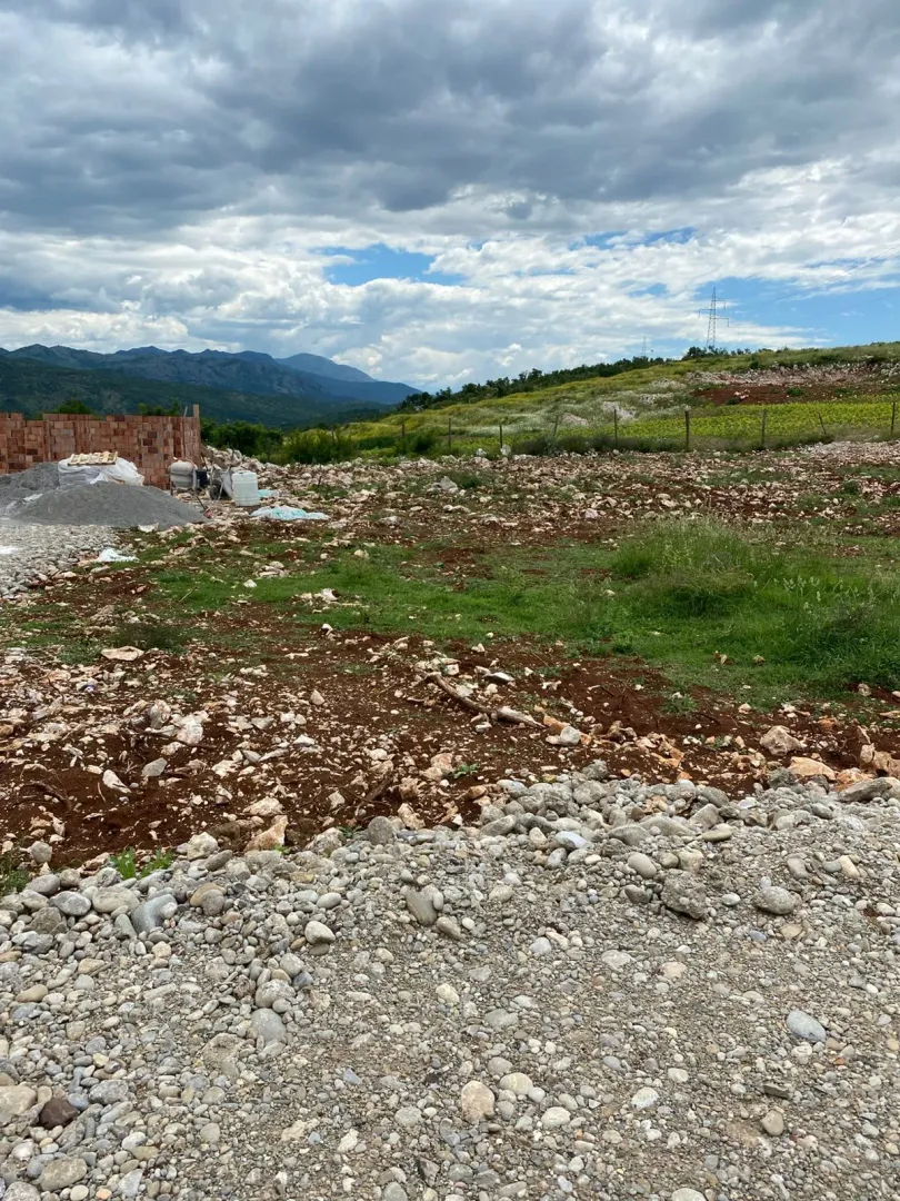 Pogled na plac sa građevinskim materijalom i okolnim brdima.