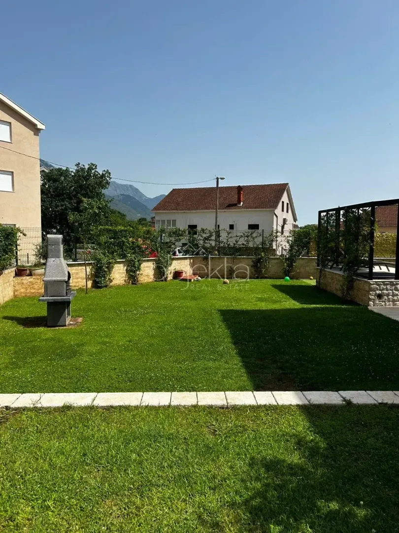 Zeleno dvorište sa travnjakom i roštiljem ispred zgrade.