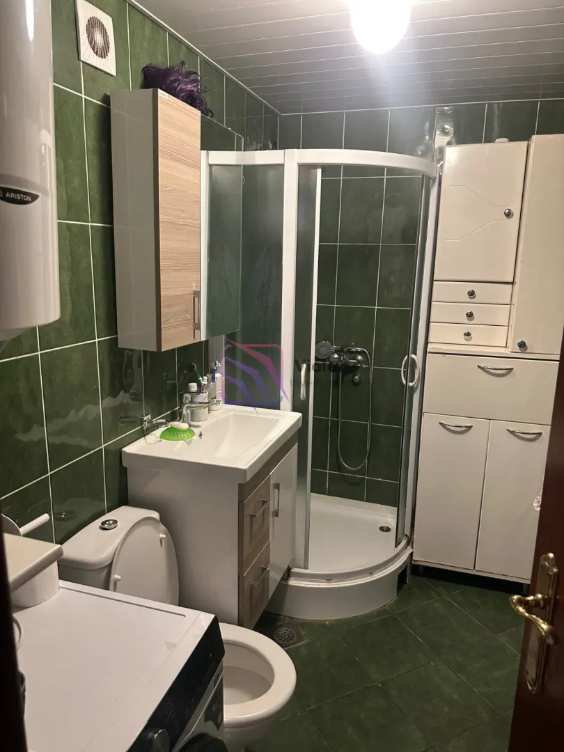 Kupatilo sa tuš kabinom, umivaonikom i bijelim ormarićima.