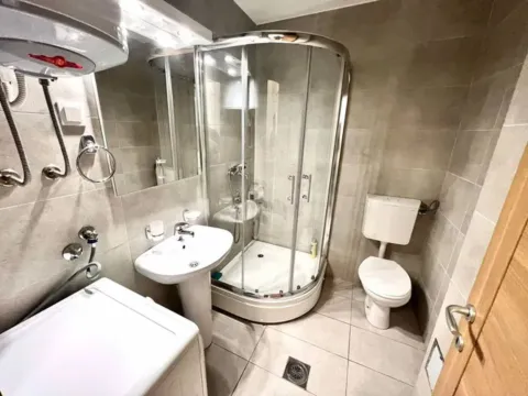 Smaller bathroom with a shower cabin, sink, toilet, and washing machine. - image 8