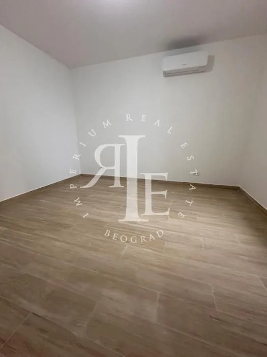 Empty room with light walls, wood flooring, and an air conditioning unit.