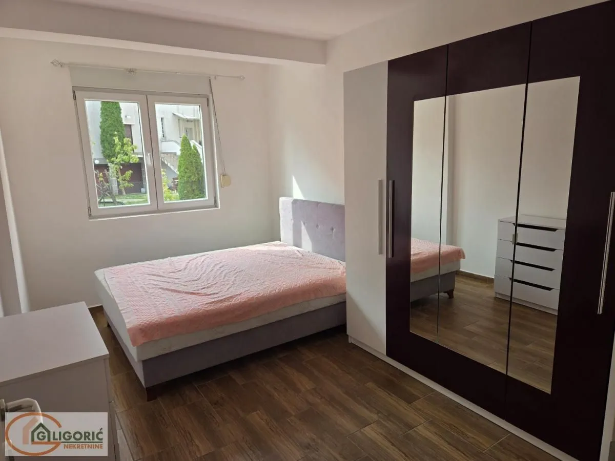 Furnished bedroom with a double bed, large mirrored wardrobe, and a window.