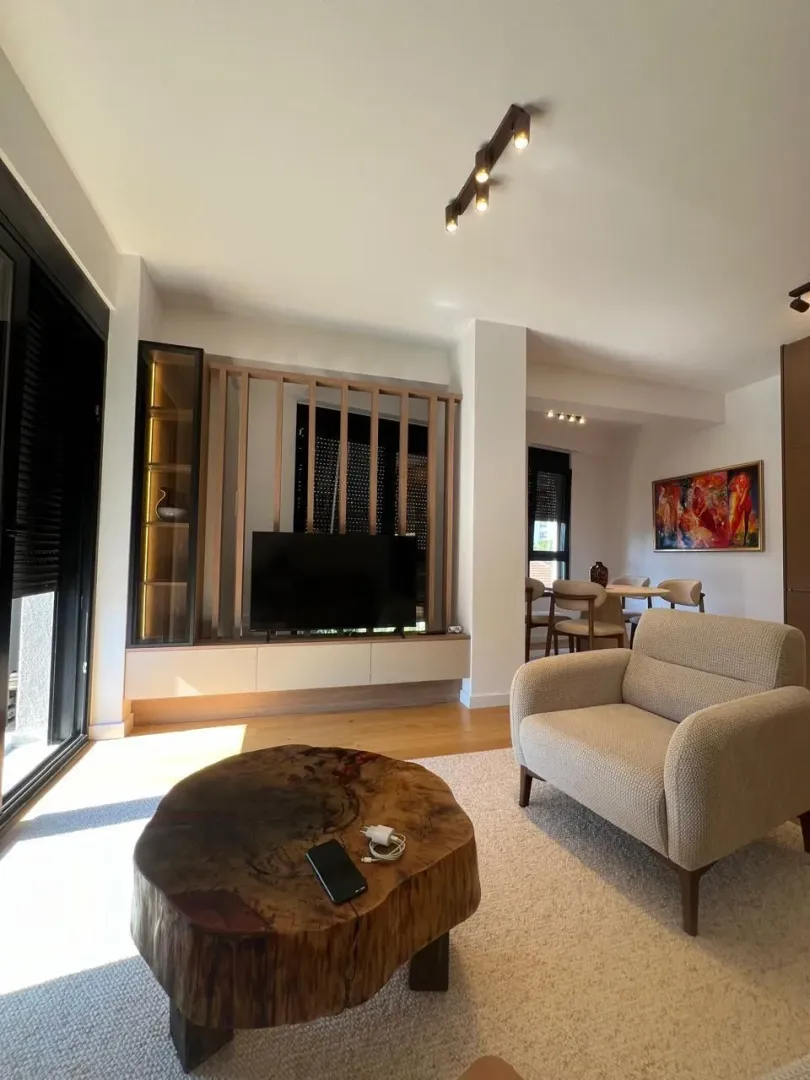Living room with armchairs, TV unit, and dining area in the background.